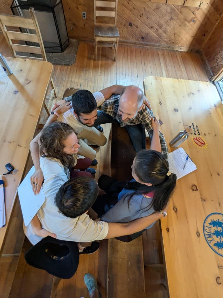 A small group of facilitators in a close huddle on a wooden floor